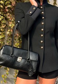 Crna strukturalna torba na rame s dvije drške, teksturirani kožni materijal, srebrni detalji i zatvaranje na kopču. Uparena s crnim sakoom s detaljima na gumbima.