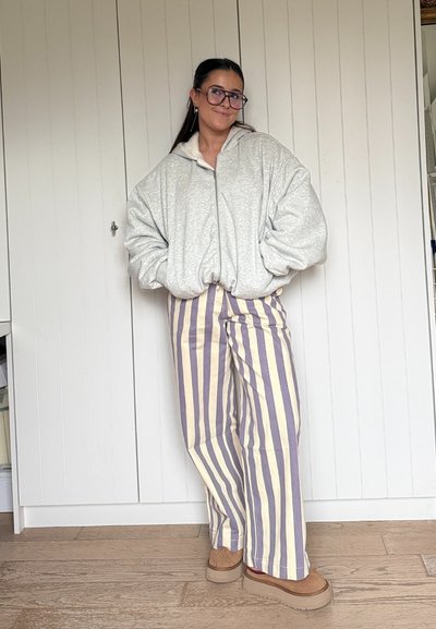 Sudadera con capucha gris claro de gran tamaño con cremallera, pantalones de pierna ancha a rayas en crema y lavanda, y zapatos marrones tipo slip-on con suela gruesa.