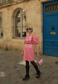  Ροζ λαμπερό φόρεμα με φουσκωτά μανίκια, λεπτομέρεια με φουσκωτό σχέδιο, μαύρες τιράντες; μαύρες μπότες πλατφόρμας μέχρι το γόνατο; παστέλ καρέ hairstyle; ροζ τσάντα.