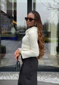 Crème, gezellige, lange mouw trui met een kraag; zwarte, aansluitende rok; zwarte cat-eye zonnebril; gouden horloge; zwarte handtas.