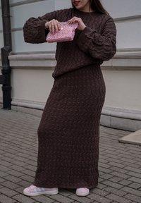 Ensemble en deux pièces marron tricoté avec un motif texturé, manches larges et jupe longue. Tenant une pochette rose à perles avec fermeture à pression.