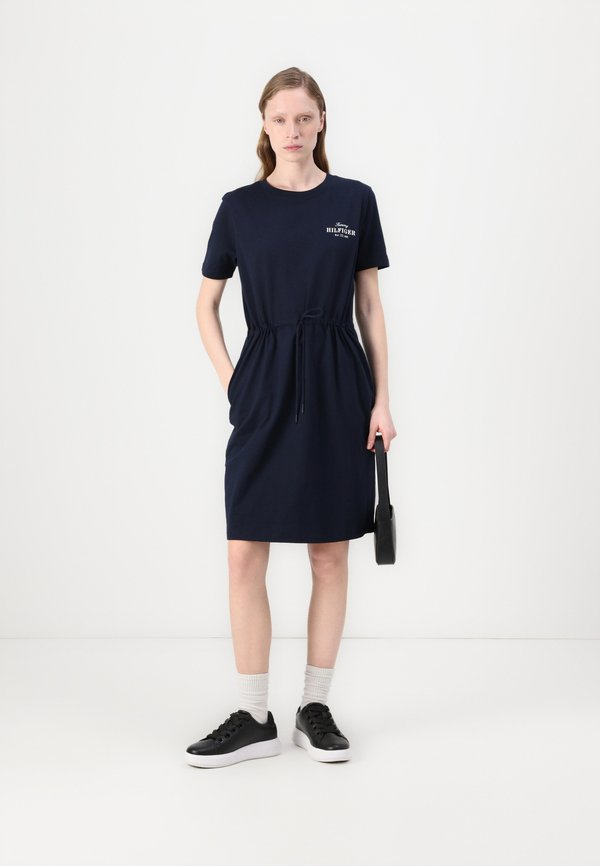 Robe en coton bleu marine à manches courtes, ceinture à cordon, poches latérales et accent de logo. Associée à des baskets noires et des chaussettes blanches.