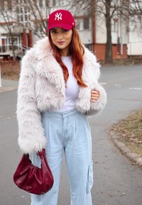 Ψεύτικη γούνα cropped μπουφάν σε ανοιχτό ροζ, συνδυασμένο με λευκή μπλούζα και ανοιχτό μπλε παντελόνι σε φαρδιά γραμμή. Διακοσμημένο με κόκκινο καπέλο και υφασμάτινη μπορντό τσάντα.