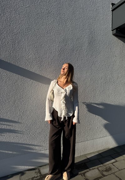 Blusa blanca con volantes y mangas largas combinada con pantalones negros de pierna ancha. Un pequeño bolso de color claro cuelga de un hombro.