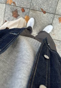 Jeansowa kurtka na lekkim swetrze i ciemnych spodniach z białymi trampkami, stojąca na kafelkowanej podłodze usłanej jesiennymi liśćmi.