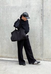 Sudadera negra de gran tamaño y pantalones de pierna ancha combinados con calzado negro con rayas blancas. Un bolso suave negro está colgado del hombro.