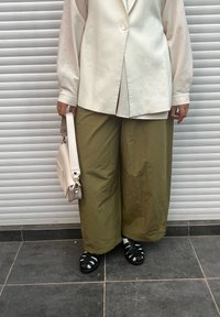 Blazer supradimensionat crem, pantaloni largi kaki, geantă albă cu curea și sandale negre cu barete, pe fundal de oblon rulant gri.