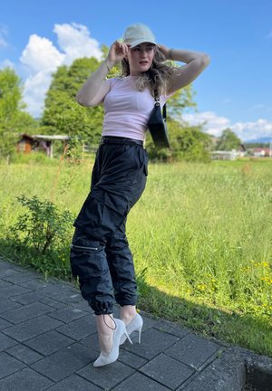 Pantalones cargo negros con bolsillos laterales, combinados con una camiseta ajustada rosa y una gorra de color claro, complementados con tacones altos blancos.
