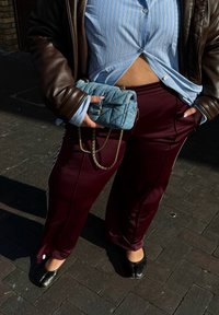 Mörkröda sportbyxor med vita ränder, en blå rutig skjorta med knappar, en brun läderjacka och en vadderad blå handväska med kedjesnodd.