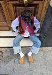 Sarkans adīts veste pār baltu kreklu, kombinēts ar plašām zilām džinsa biksēm un brūnām kurpēm bez auklām. Aksesuāri ietver zilu šalli un brūnu somu.