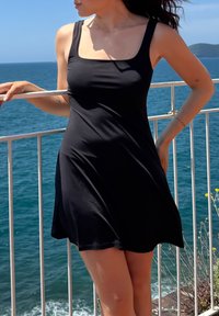 Vestido preto sem mangas com decote quadrado, feito de um tecido leve e fluido. A bainha atinge a metade da coxa e tem um corte solto.