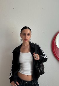 Must-haves mustriline, valge triibuga must zip-up kapuutsiga särk, valge tank top, tumedad teksad ja must käekott. Hõbedased rõngastükid ja sõrmused. Taustal punane ümmargune peegel.