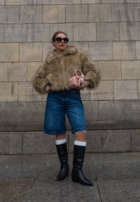 Ψεύτικη γούνα μπεζ ζακέτα, μπλε τζιν σορτς, μαύρες μπότες μέχρι το γόνατο με άσπρες μανσέτες, στιλάτη ροζ τσάντα χειρός, υπερμεγέθη μαύρα γυαλιά ηλίου.