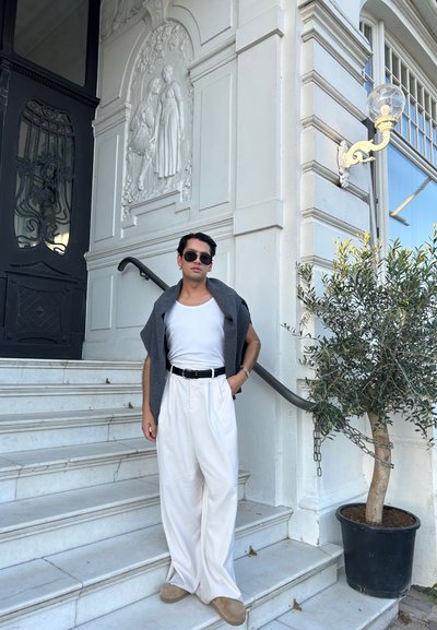 Pantalones de pierna ancha blancos combinados con una camiseta ajustada blanca y un suéter gris caído sobre los hombros. Cinturón negro y calzado informal.