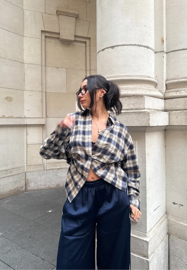 Chemise en flanelle à carreaux bleu et crème, ample avec un nœud à l'avant, associée à un pantalon large bleu marine foncé.