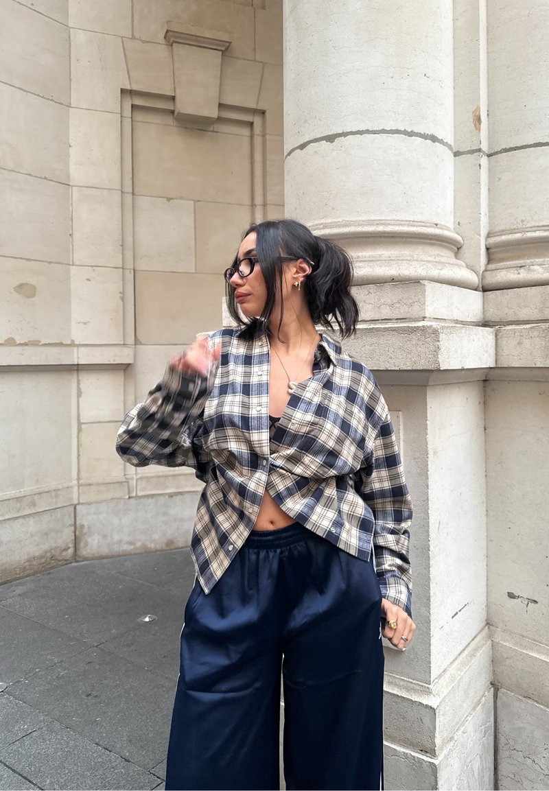 Chemise en flanelle à carreaux bleu et crème, ample avec un nœud à l'avant, associée à un pantalon large bleu marine foncé.