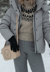 Casaco puffer cinza claro, suéter de malha bege com padrão, calças de malha cinza, luvas pretas e uma bolsa de ombro bege texturizada.