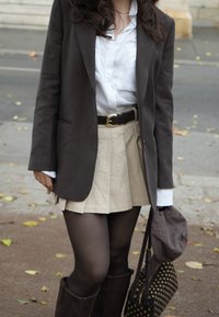 Smeđi sako, bijela košulja, bež suknja, tamne hulahopke, smeđe čizme do koljena i crna torba s rupicama. Ležerna odjevna kombinacija s nekoliko slojeva.