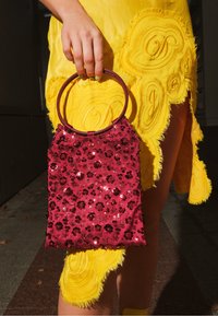 Sac à main rouge avec sequins et motifs floraux, de forme rectangulaire avec une anse circulaire, assorti à une robe jaune à franges.