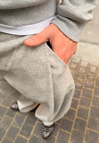 Pilkos, minkštos medvilninės laisvalaikio keln�ės su laisvu siluetu, turinčios šoninę kišenę. Matoma balta juosmens juosta ir kartu dėvimi rudi oficialūs batai.