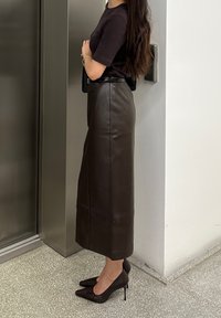 Brun læder midi-nederdel med en lige form, sort bælte og en glat overflade. Båret med sorte spidse højhælede sko.