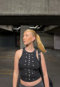 Crop top negru cu cordon ondulat, având detalii cu capse argintii, asociat cu pantaloni raiati, într-o structură de parcare din beton cu accente metalice.