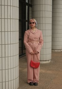 Rosa drakt med skreddersydd jakke og vide bukser, sammen med en rød håndveske. Har klumpete svarte platåsko.