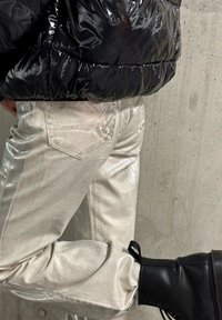 Metalické stříbrné džíny s lesklým povrchem, obsahující zadní kapsy a slim fit, spárované s černými kotníkovými botami a lesklou černou péřovkou.