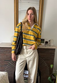 Gelb-grün gestreiftes Langarmshirt mit einem weißen Kragen, kombiniert mit ivoryfarbene weitem Hosen und einer strukturierten schwarzen Tasche.