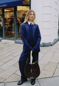 Σκούρο μπλε κοστούμι με ρίγες, συνδυασμένο με μπλε πουλόβερ και ροζ πουκάμισο με γιακά, συνοδευόμενο από σκούρο καφέ τσάντα ώμου και μαύρα μποτάκια μέχρι τον αστράγαλο.