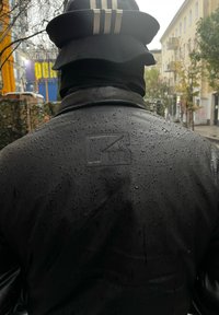 Svart vattentät jacka med en diskret logodetalj på baksidan, med en slät yta och vattendroppar synliga på dess yta.