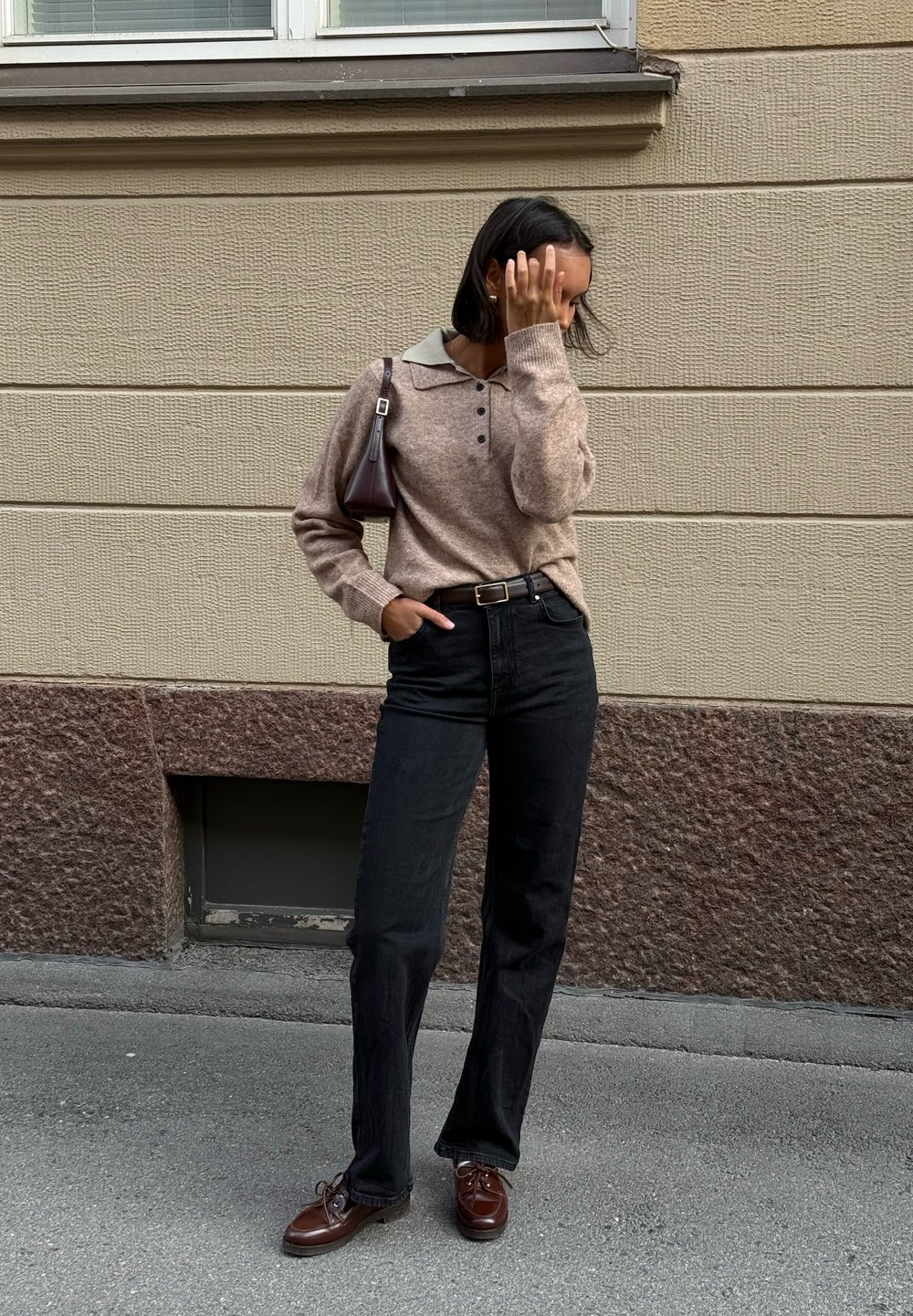 Bruine gebreide trui met een grijze kraag, zwarte high-waisted jeans en bruine veterschoenen. Een kleine bruine handtas maakt de outfit compleet.