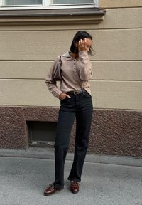 Bruine gebreide trui met een grijze kraag, zwarte high-waisted jeans en bruine veterschoenen. Een kleine bruine handtas maakt de outfit compleet.