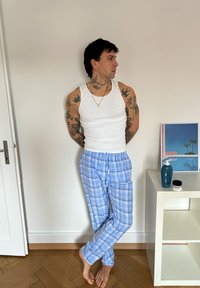 Witte geribbelde tanktop gedragen met blauwe geruite pyjamabroek. De kamer heeft een houten vloer en een kleine tafel met huidverzorgingsproducten en kunstwerken.