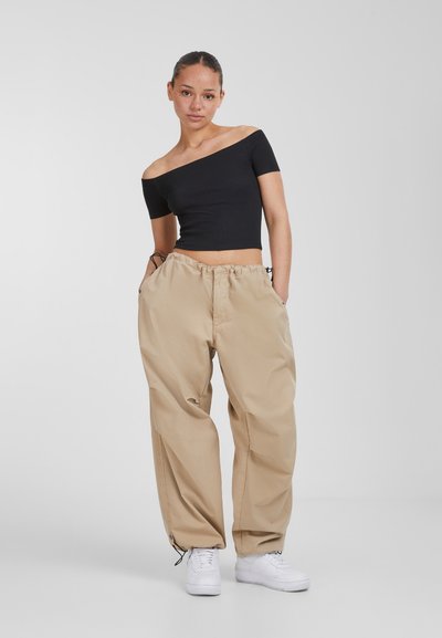 Top corto de canalé negro sin mangas combinado con pantalones cargo beige holgados. Zapatillas blancas completan el conjunto, que incluye una cinturilla elástica.