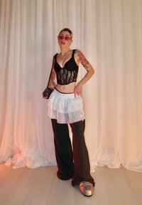 Haut court en dentelle noire, jupe blanche superposée, pantalons larges noirs et chaussures plateformes argentées métalliques. Tissu transparent avec un motif texturé.