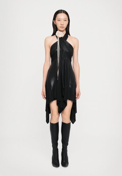 Vestido negro de tirantes con dobladillo asimétrico, tela drapeada y acento floral en el cuello. Combinado con botas negras hasta la rodilla, de textura suave.