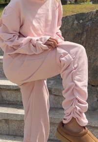Lichtroze, oversized sweatshirt met lange mouwen, gecombineerd met bijpassende, gerimpelde broek. Zachte stof, ontspannen pasvorm en textuurdetails.
