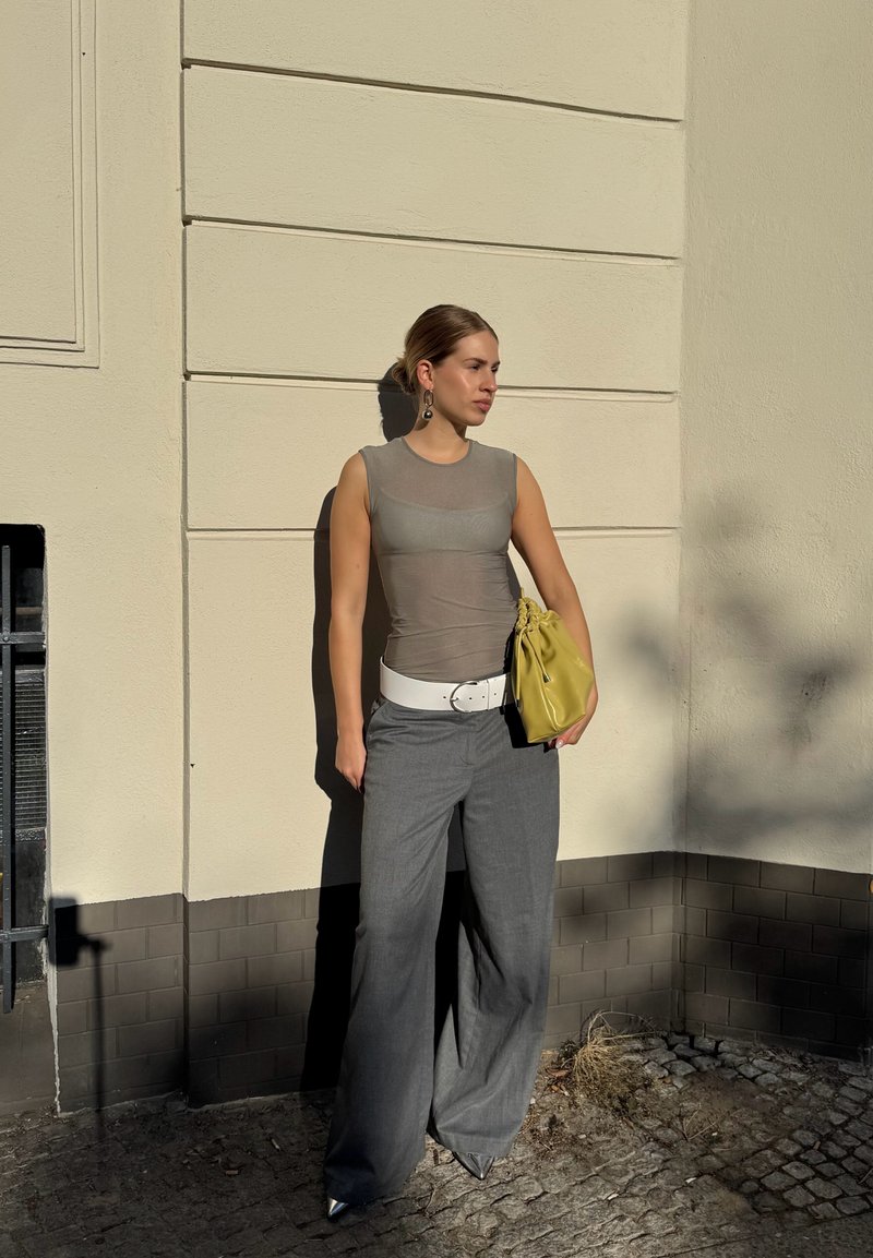 Pantalon large gris, haut gris transparent, ceinture blanche et sac en cuir jaune. Des talons argentés pointus et de grandes boucles d'oreilles complètent le look.