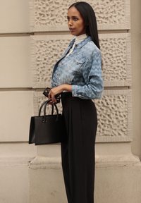 Világoskék, zigzag mintás farmerdzseki, fekete, magas derekú nadrággal párosítva. Egy kis, sima textúrájú fekete kézitáskát tart a kezében.