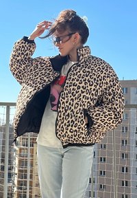 Pufferjack met luipaardprint, voorzien van een ritsluiting, zwarte accenten en een hoge kraag. Gelaagd over een graphic t-shirt en lichte jeans.