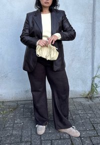 Black leather blazer over a light yellow top, paired with black wide-leg pants and beige sneakers. Holding a soft, cream-colored handbag.