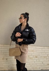 Μαύρο μπουφάν με ψηλό γιακά, καφέ πλεκτό φόρεμα, τσάντα σε χιαστί σχέδιο και μαύρες μπότες μέχρι το γόνατο. Τα αξεσουάρ περιλαμβάνουν γυαλιά ηλίου και σκουλαρίκια.