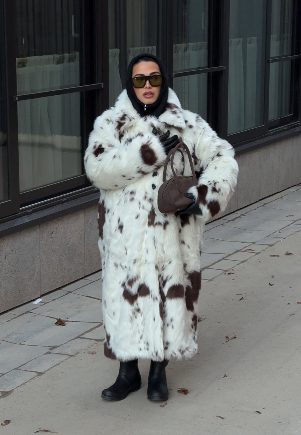 Fehér bolyhos kabát barna foltokkal, fekete ruházat és kesztyű fölött viselve. A megjelenést fekete csizmák és egy kis barna kézitáska egészíti ki.