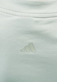 Vaaleanvihreä collegekangas, jossa on sileä pinta ja kohoava valkoinen Adidas-logo, joka koostuu kolmesta vinosta raidasta.