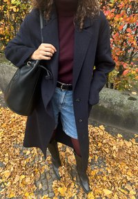 Mornarsko volneno plašč nad burgundskim puloverjem z visokim ovratnikom, modri denim kratki hlači in črne škornje do kolen. Dodatki vključujejo črno torbico v obliki vedra.