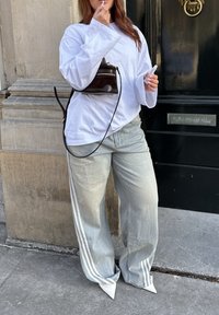 Hvid oversized langærmet t-shirt, lyseblå brede jeans med hvide striber, og spidse hvide sko. Lille sort håndtaske med en rem.