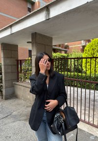 Czarny, oversize'owy żakiet z poduszkami na ramionach, noszony na białym topie, w połączeniu z jasnoniebieskimi dżinsami. Trzyma czarną torbę z srebrnymi dodatkami.