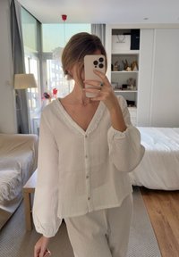 Bluză albă, texturată, cu guler în V, guler volan, și mâneci bufante, asortată cu pantaloni dintr-o țesătur�ă ușoară.