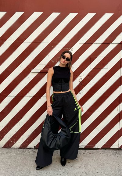 Top negro corto sobre un corsé estructurado, combinado con pantalones negros holgados con franjas verde neón. Bolso negro y gafas de sol.